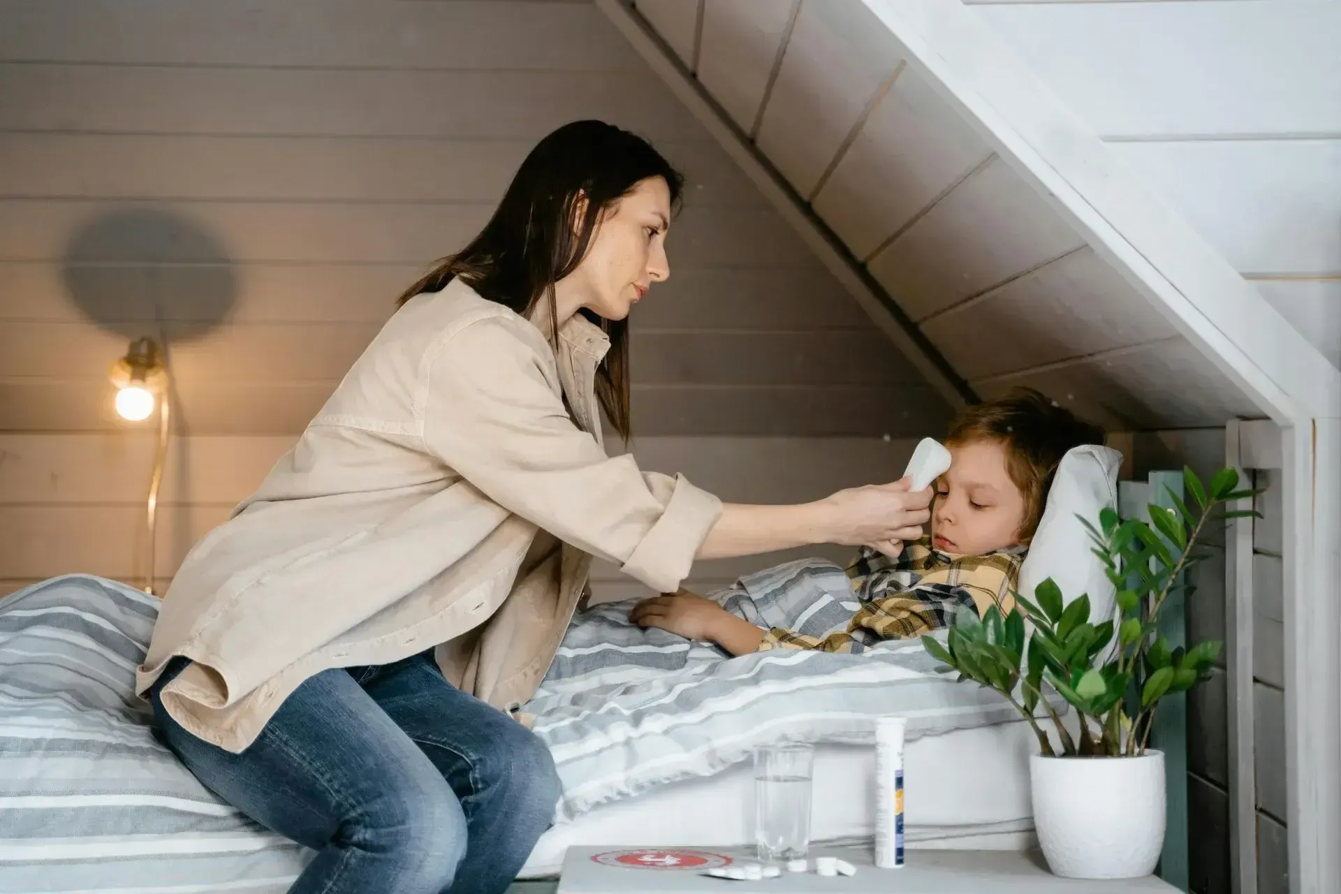 A mother gently brushes her child's teeth in bed, promoting good hygiene during cold, flu, or allergy season.