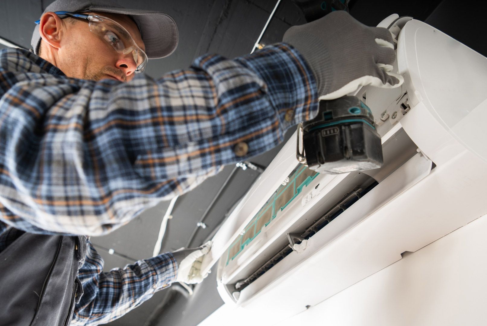 A man is working on an air conditioner with a drill.