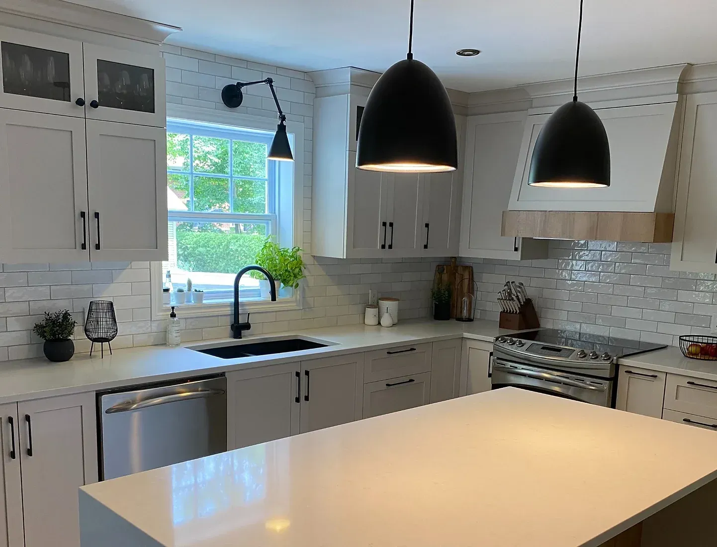 Cuisine moderne avec armoires blanches, îlot et luminaires suspendus noirs.