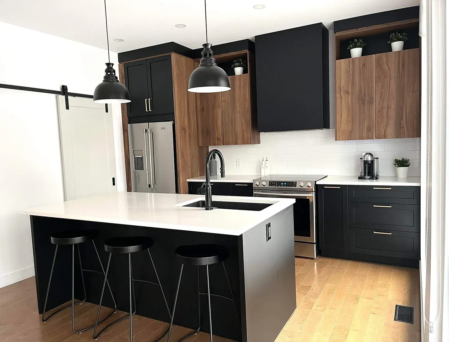 Cuisine moderne : îlot noir avec tabourets, armoires en bois et noires, électroménagers en acier inoxydable.