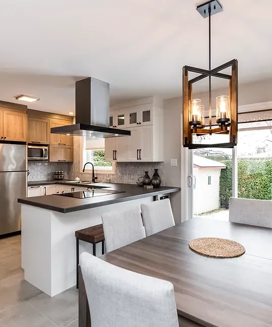 Cuisine avec coin repas : luminaire, armoires, îlot, table, chaises et électroménagers en acier inoxydable.