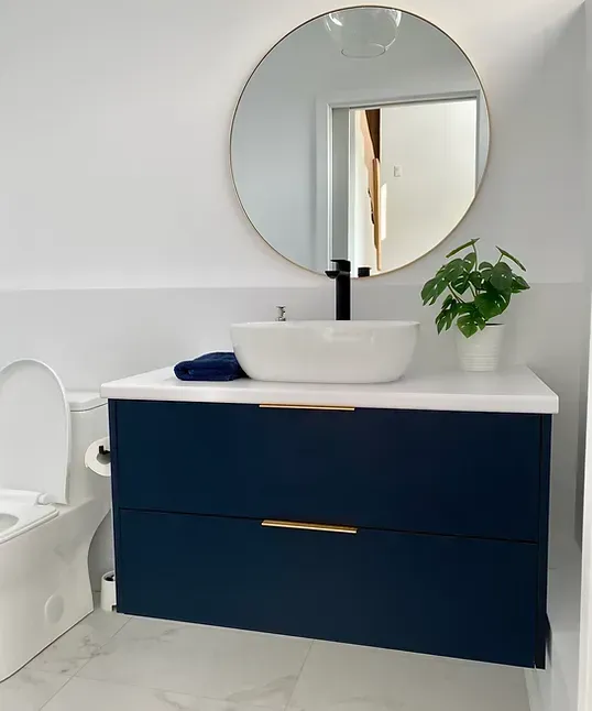 Meuble-lavabo bleu marine avec un comptoir blanc, un miroir rond et une plante en pot.