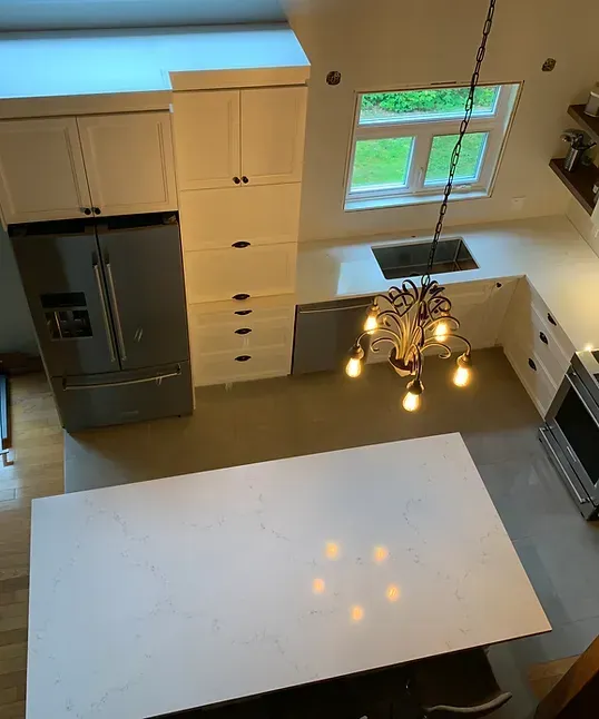 Vue en plongée d'une cuisine moderne avec un grand îlot, des appareils en acier inoxydable et un lustre.