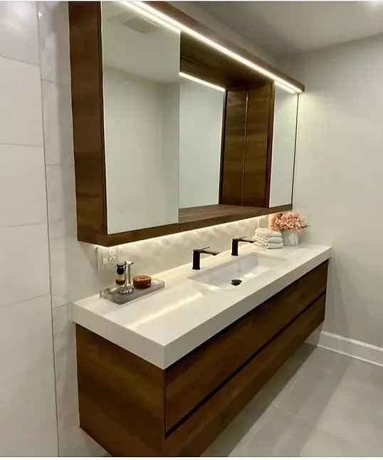 Salle de bain moderne avec meuble-lavabo en bois, plan de travail blanc et grand miroir. Elle comprend également des accessoires noirs et une composition florale.