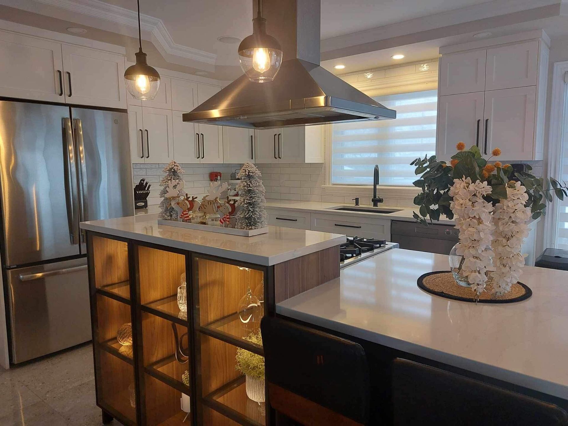 Cuisine moderne avec armoires blanches, électroménagers en acier inoxydable, îlot avec étagères en bois et luminaires suspendus.