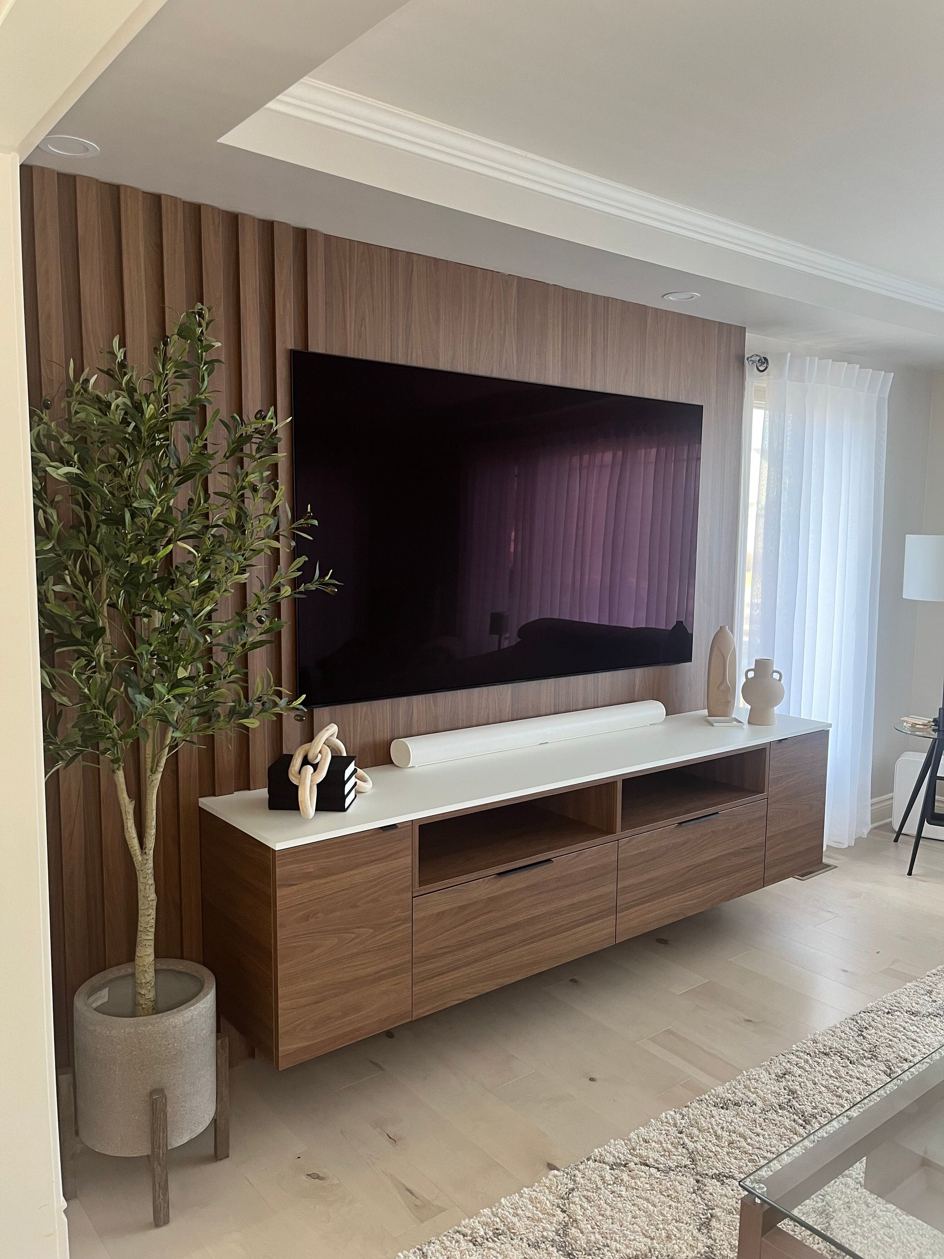 Salon avec mur d'accent lambrissé, grande télévision, console flottante, olivier et fenêtre lumineuse.