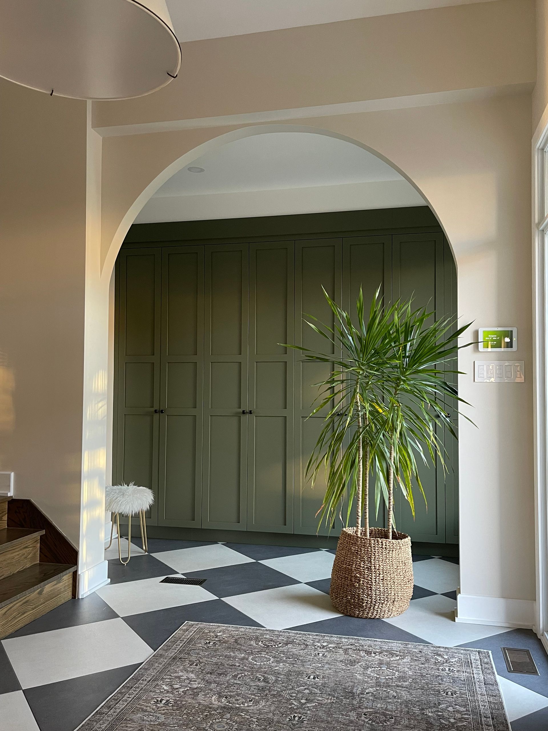 Intérieur avec porte en arc, sol en damier, armoires de rangement vertes et plante en pot.