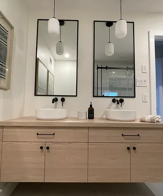 Meuble-lavabo flottant en bois clair avec deux lavabos, miroirs et luminaires noirs.