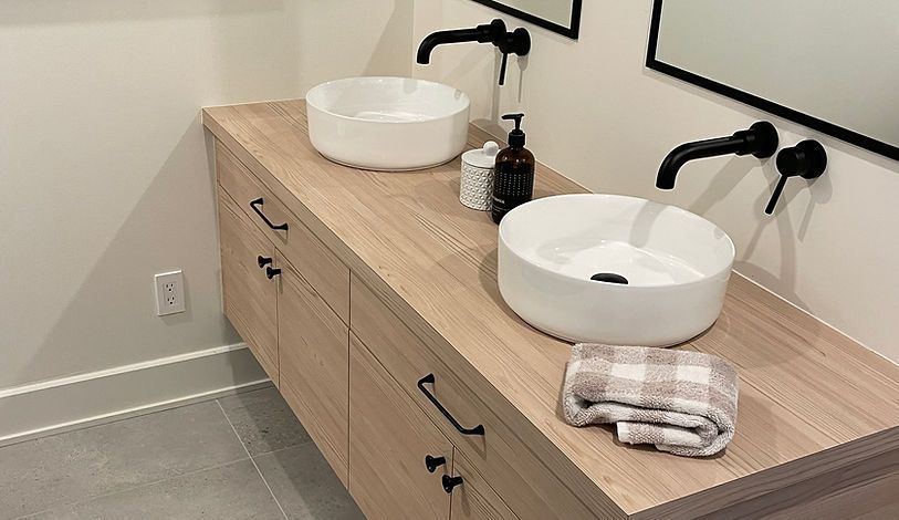 Un meuble-lavabo avec deux vasques blanches, des robinets noirs et des tiroirs en bois. Une serviette à carreaux est pliée à proximité.