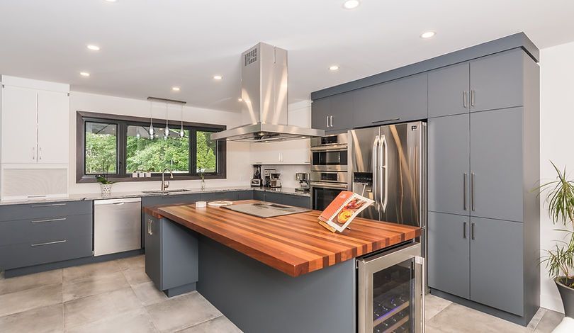 Cuisine moderne avec armoires grises, comptoir en îlot de bois, électroménagers en acier inoxydable et fenêtre donnant sur la verdure.