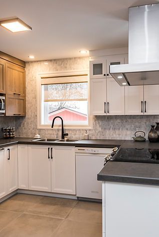 Cuisine moderne avec armoires blanches et en bois, comptoirs noirs et une fenêtre avec une maison rouge visible.