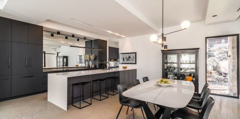 Cuisine et salle à manger modernes avec armoires foncées, îlot et table en marbre blanc.
