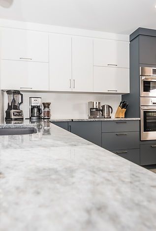 Cuisine moderne avec armoires blanches et grises, comptoirs en granit et appareils électroménagers.