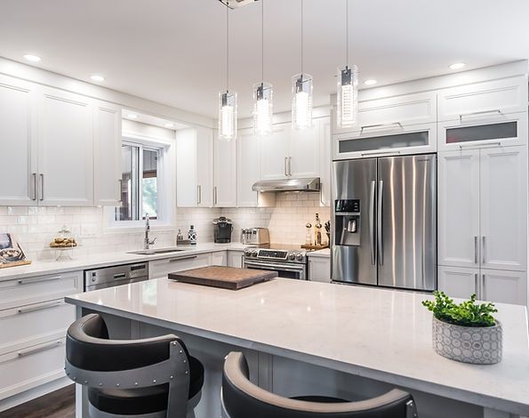 Cuisine moderne blanche et lumineuse avec îlot, appareils électroménagers en acier inoxydable et luminaires suspendus.