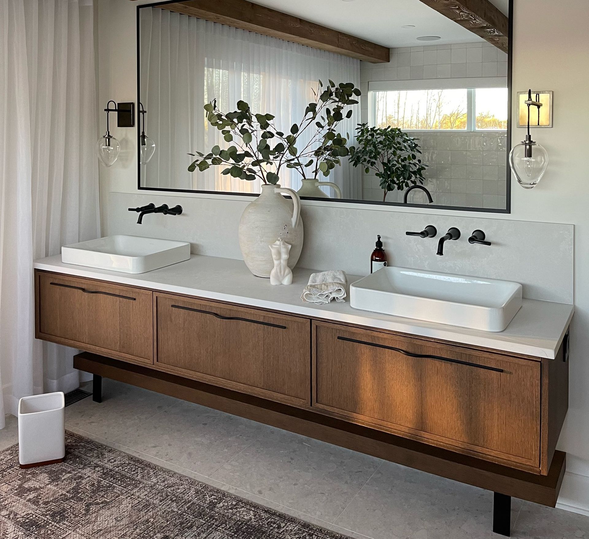 Salle de bain moderne avec vanité en bois, lavabos blancs, luminaires noirs et grand miroir.