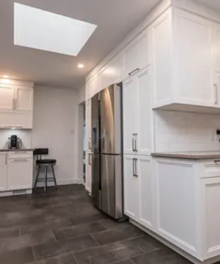 Cuisine blanche avec réfrigérateur en acier inoxydable, sol en ardoise et puits de lumière.