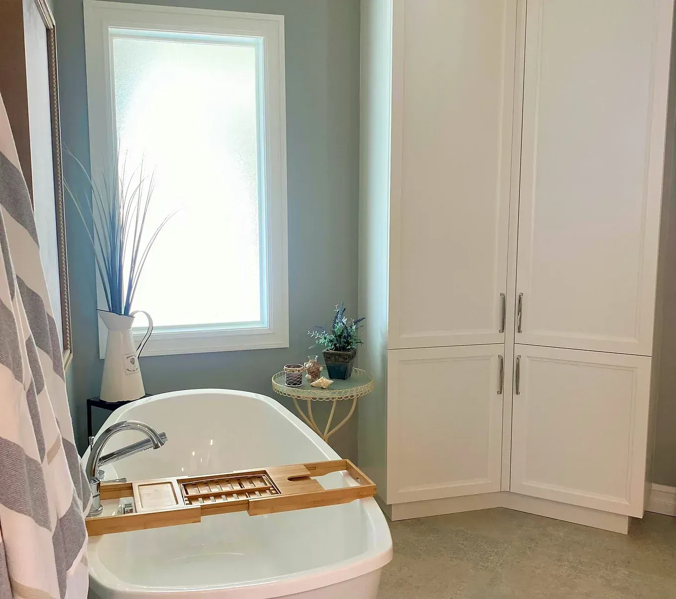 Une baignoire blanche dans une salle de bain avec des armoires blanches, une fenêtre et des objets décoratifs.