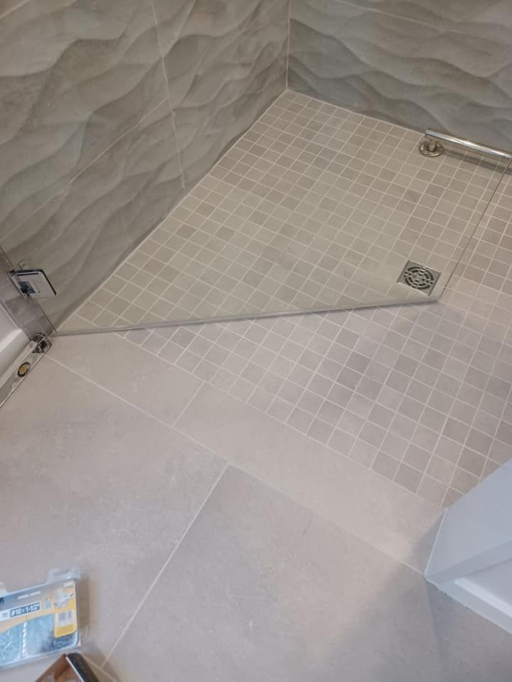 Shower with gray tile walls, and a tiled floor. Glass shower door.