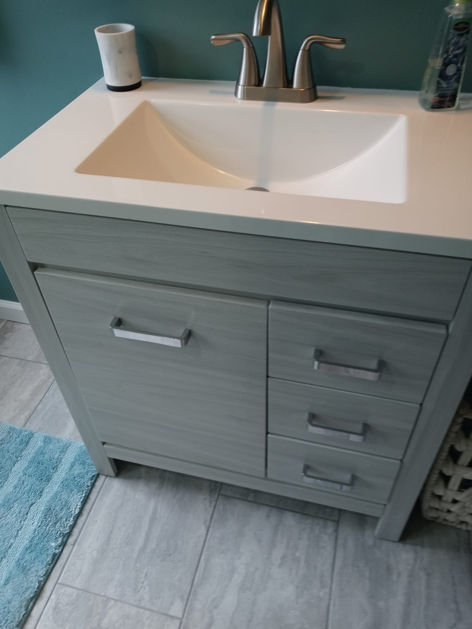 Gray bathroom vanity with sink and faucet, white countertop, and three drawers.