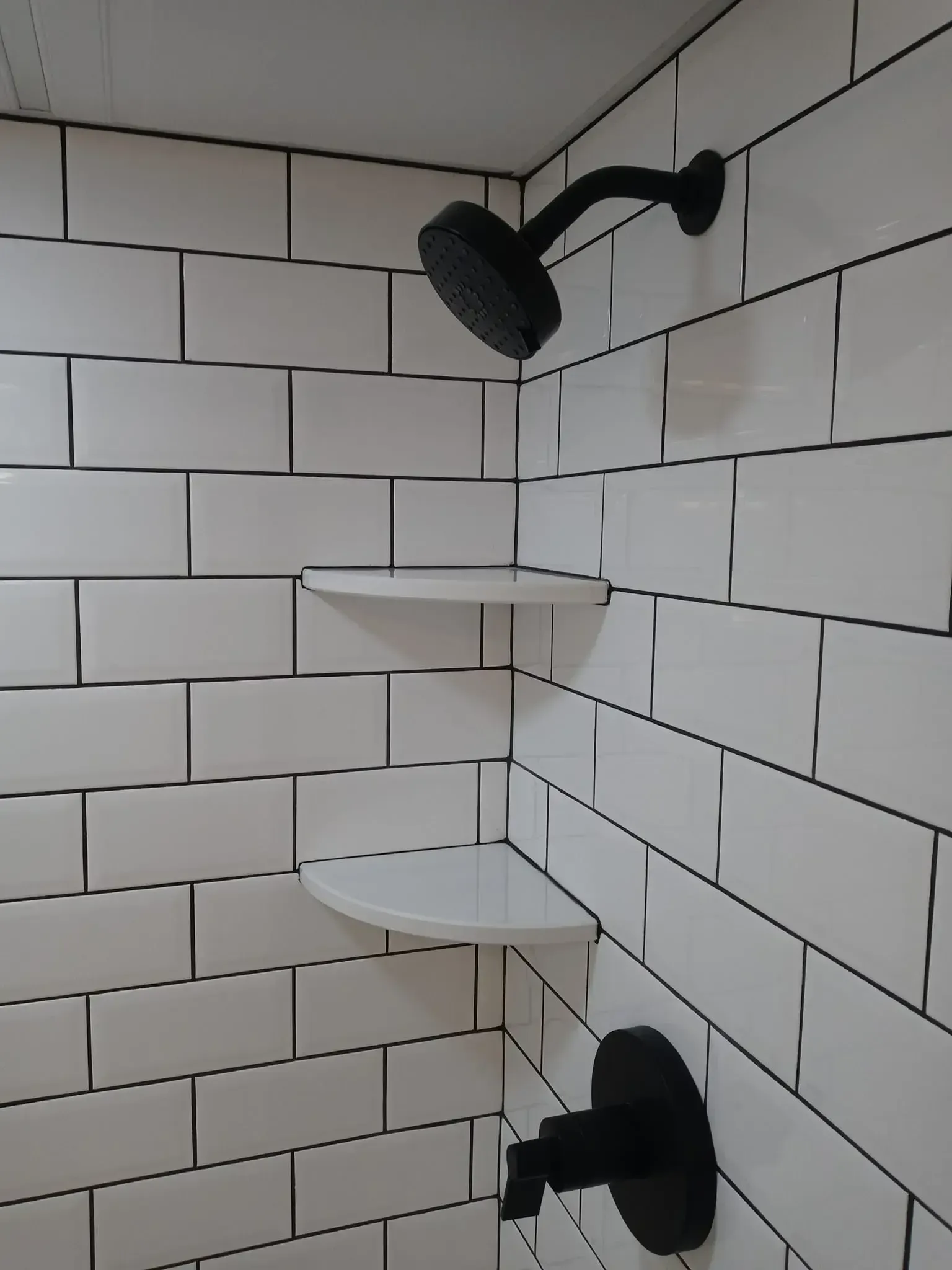 White tiled shower with black showerhead, shelves, and faucet.