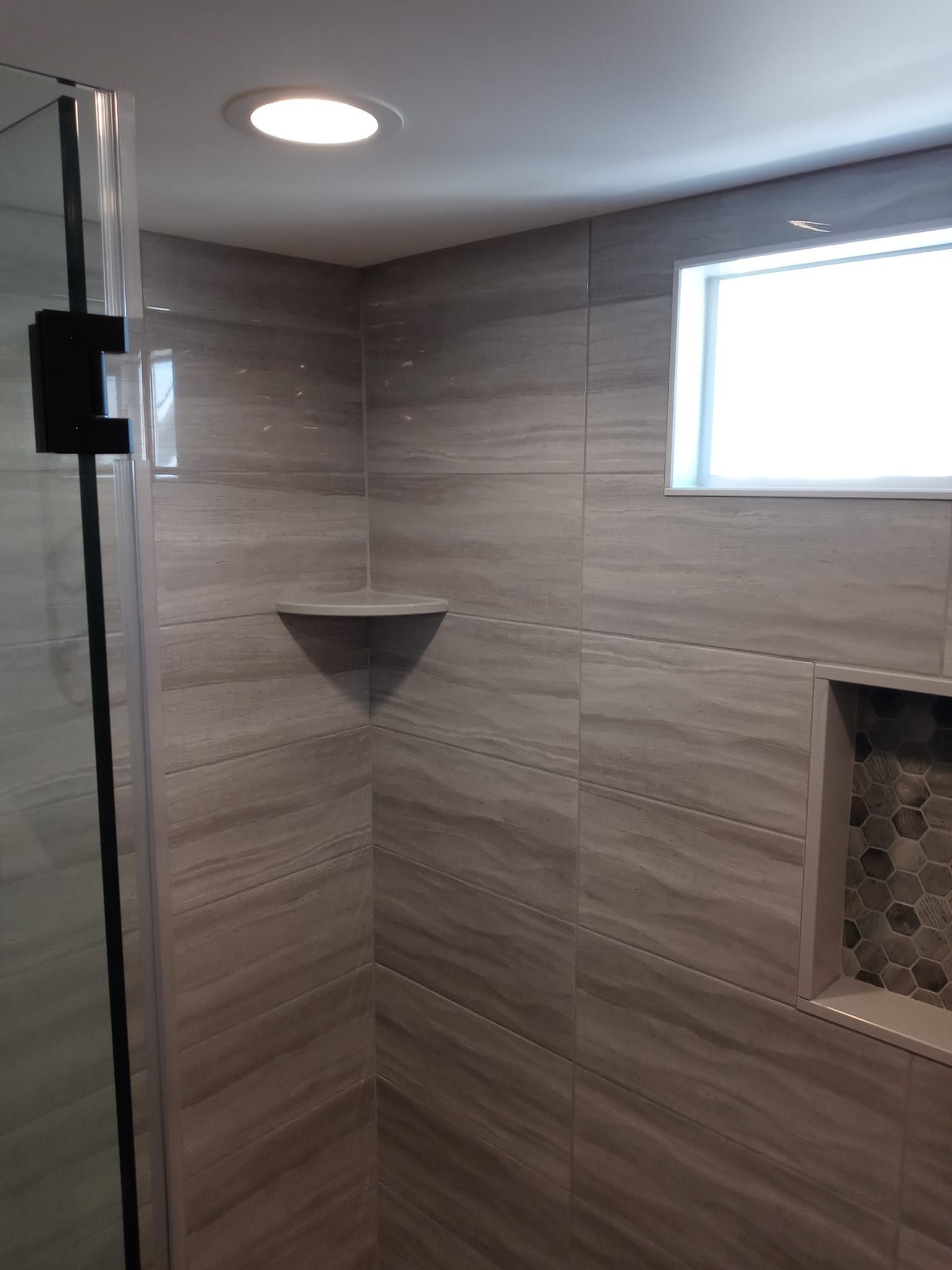 Bathroom interior with gray tiled walls, shower enclosure, built-in shelf, and recessed storage.