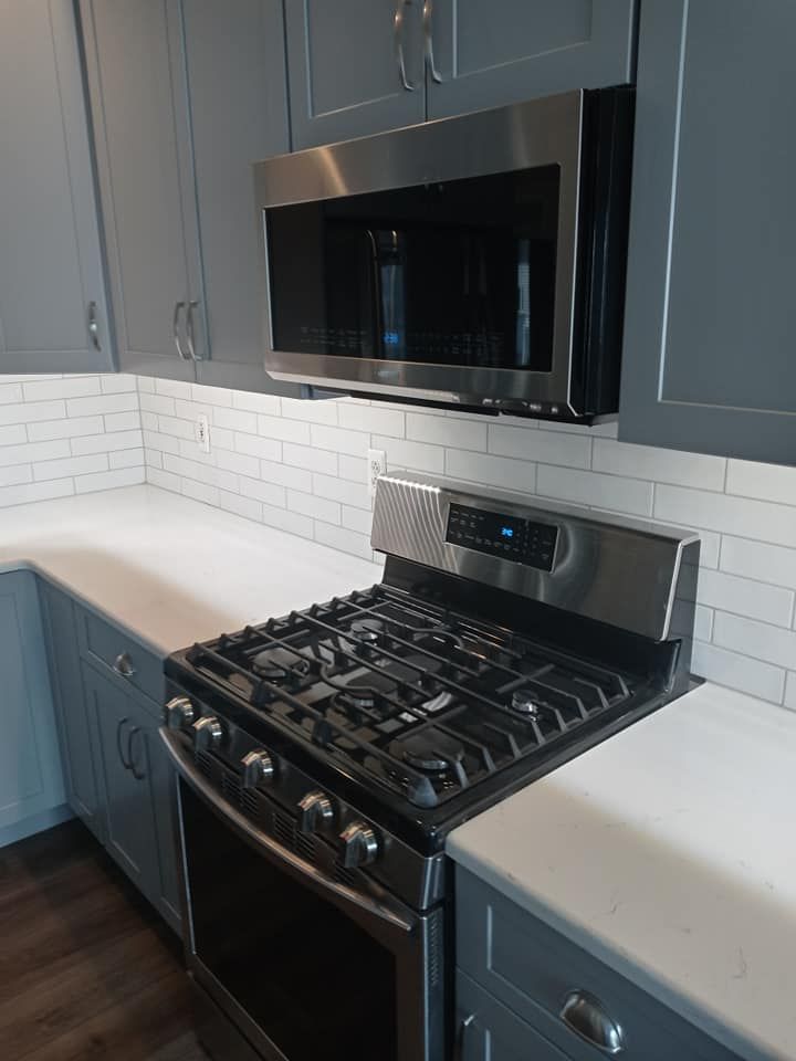 Stainless steel gas range and microwave in gray kitchen with white countertops.