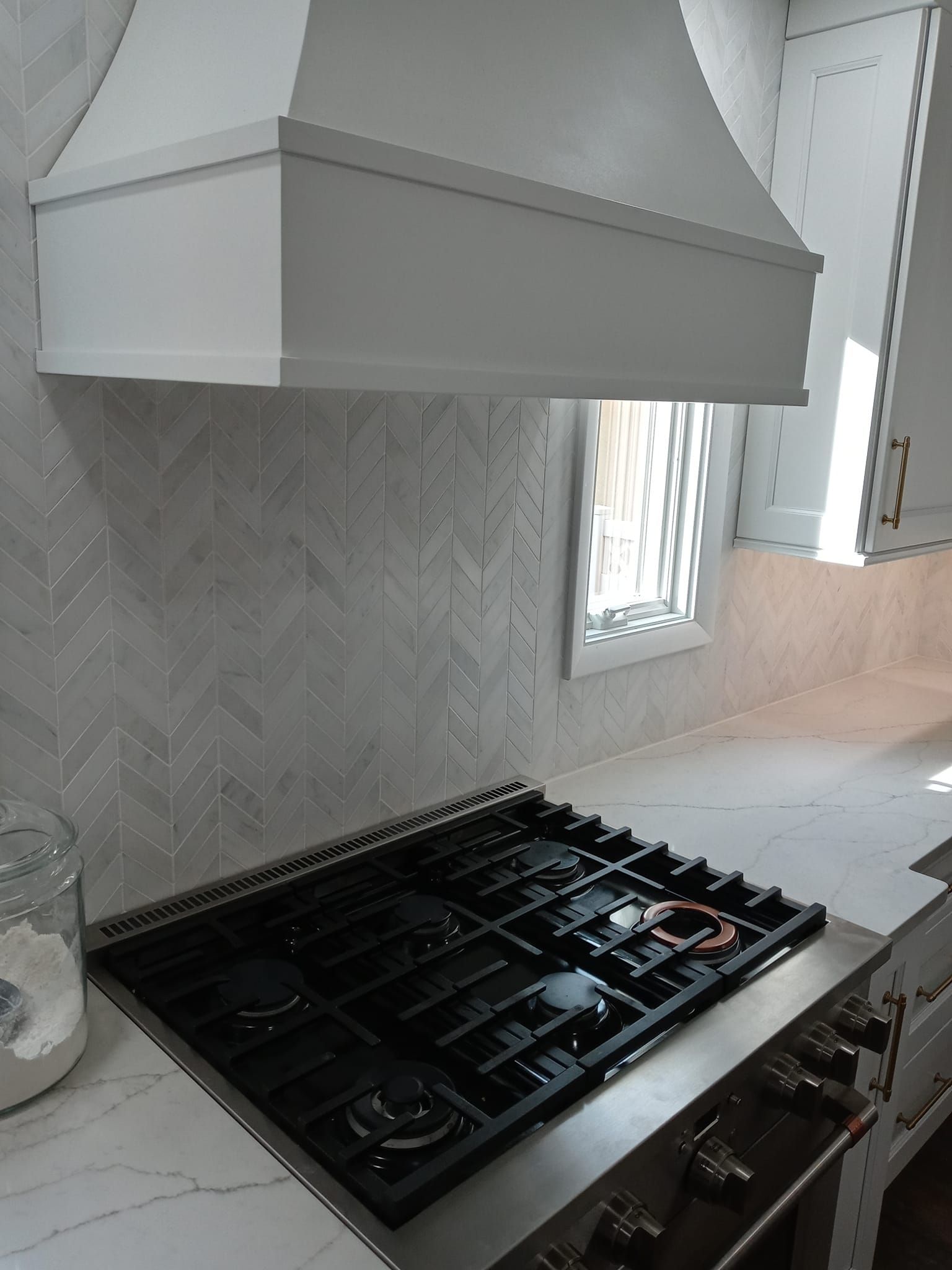 Kitchen with a stove, range hood, and light-colored backsplash and countertops.
