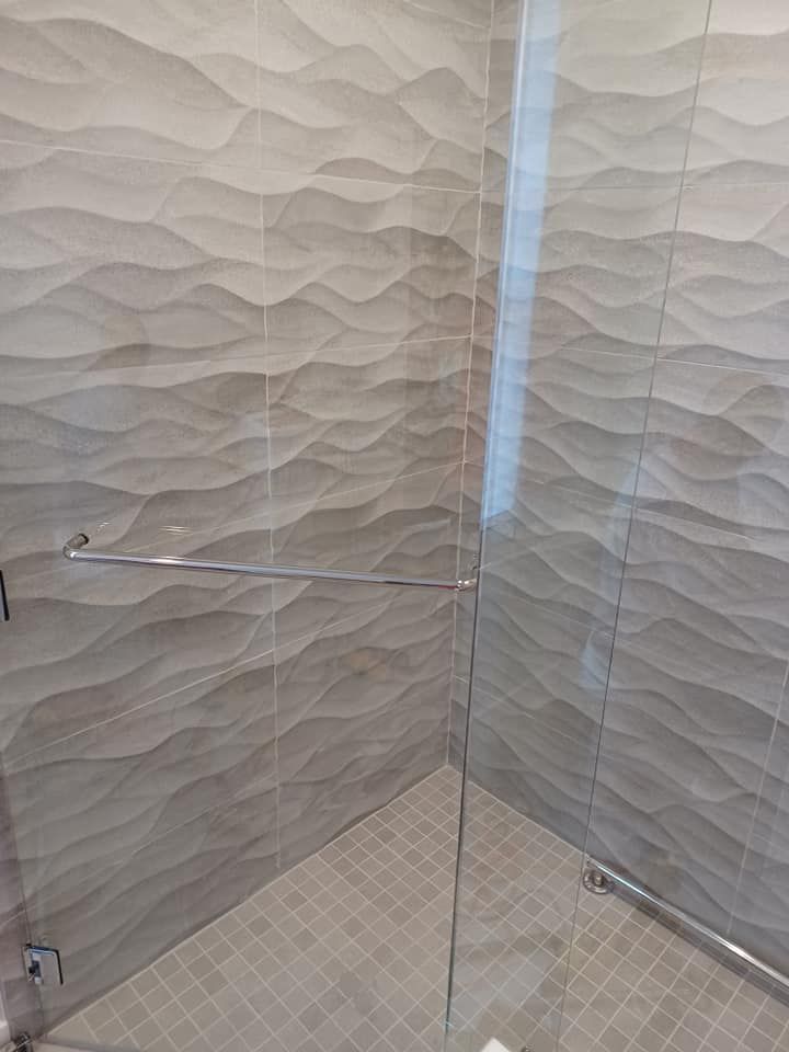 Shower with gray wave-patterned tile walls, glass door, and a grab bar.