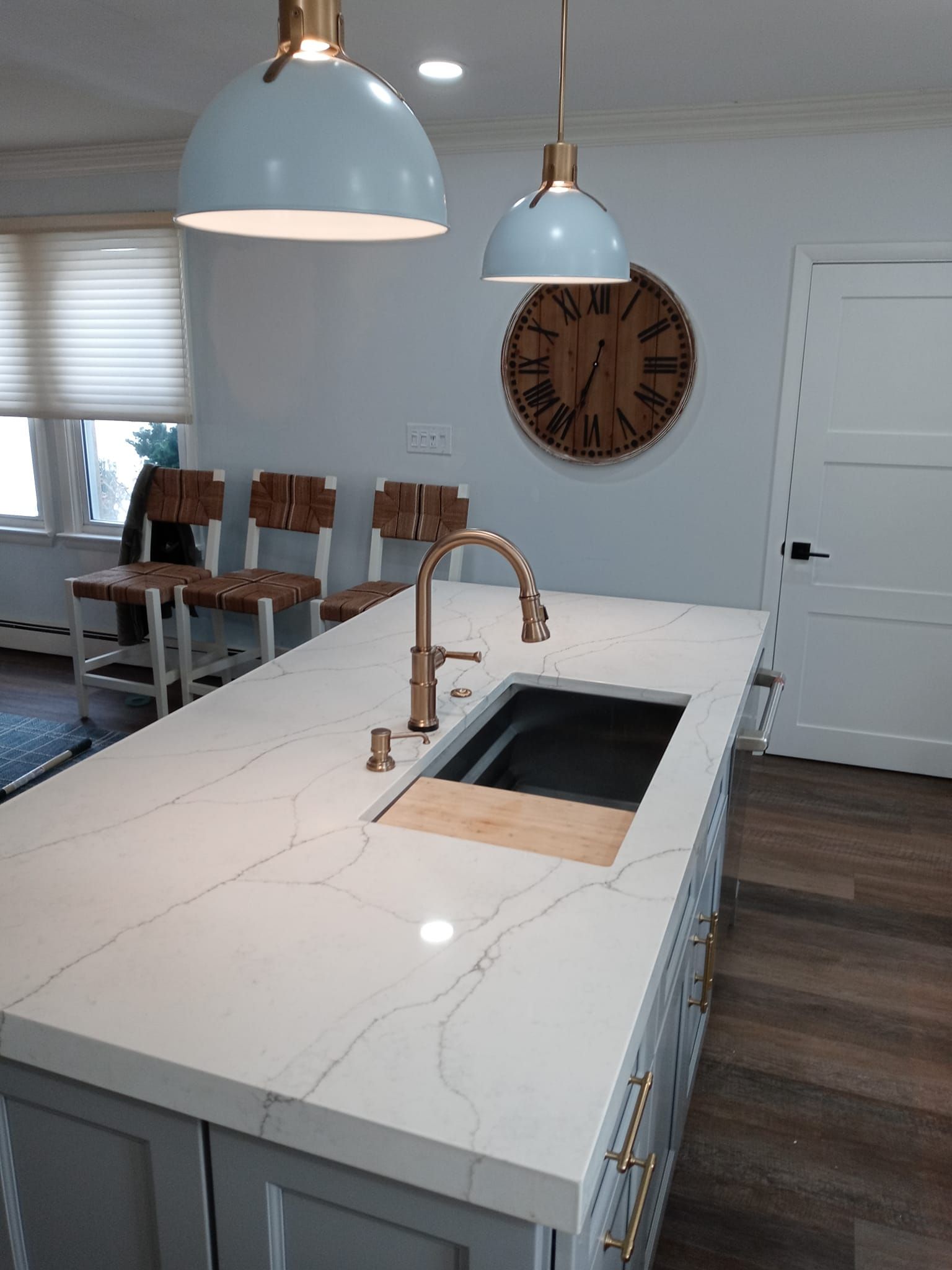 Kitchen island with copper faucet, sink, and wood cutting board. Light blue pendant lights hang above.