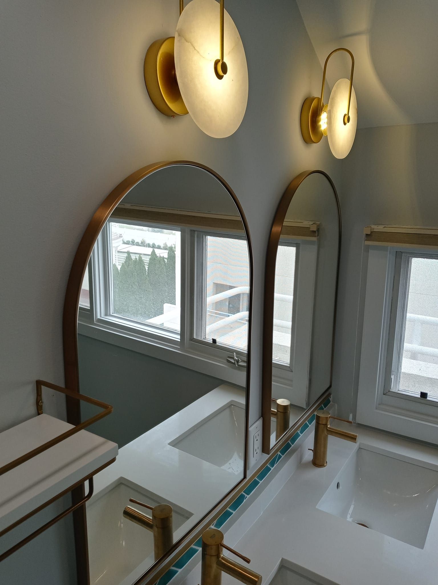 Bathroom with two arched mirrors, gold fixtures, and disk-shaped sconces.