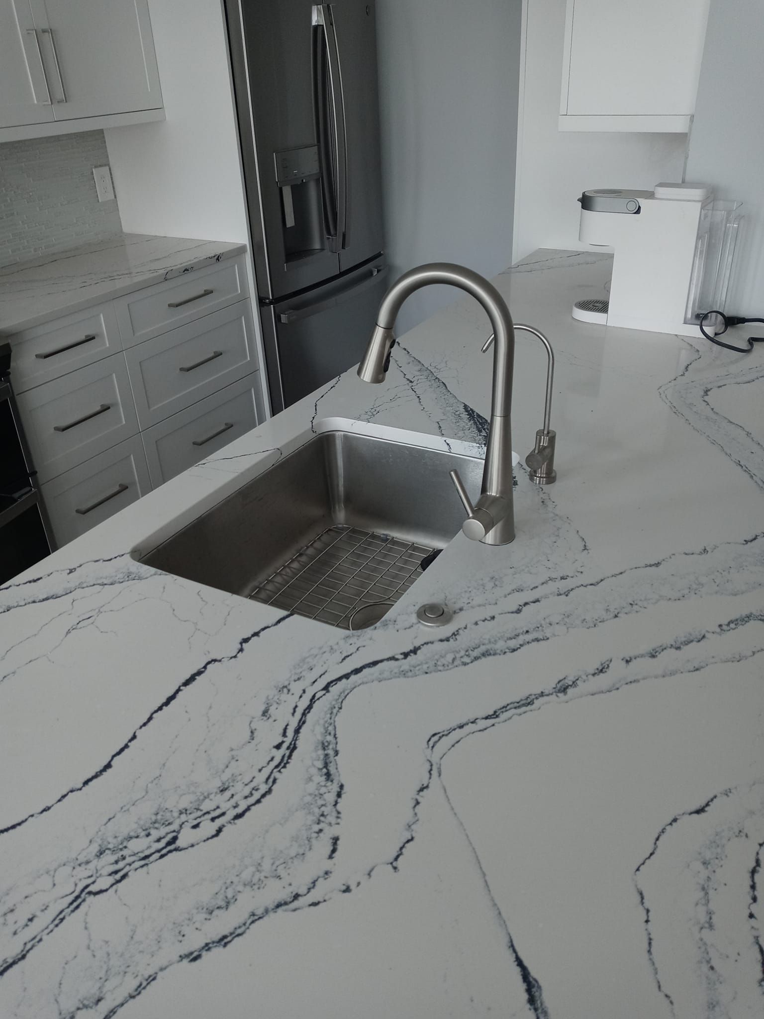 Stainless steel sink with faucet in a modern kitchen with white and gray countertops.