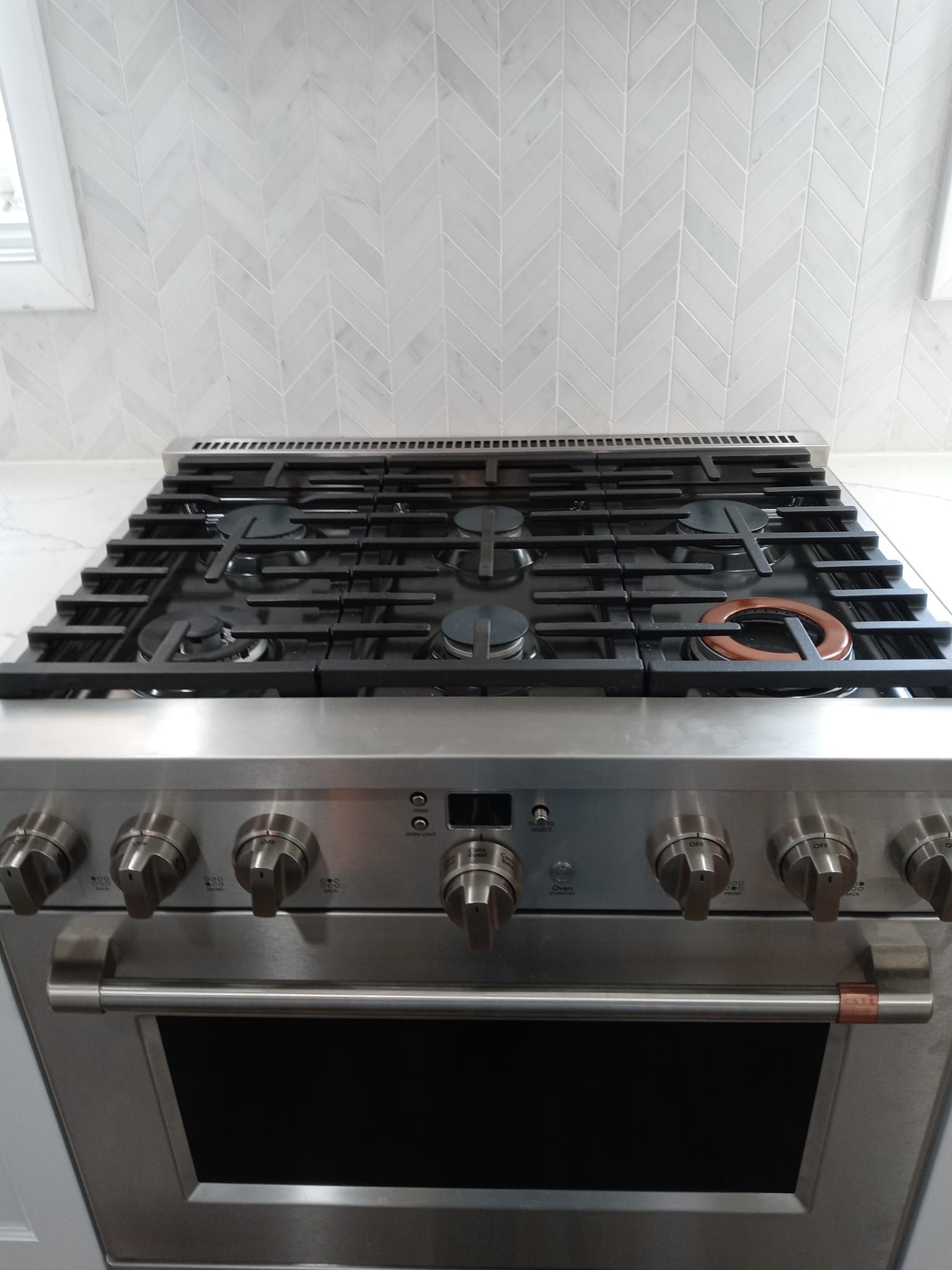 Stainless steel gas range in kitchen with white herringbone backsplash.