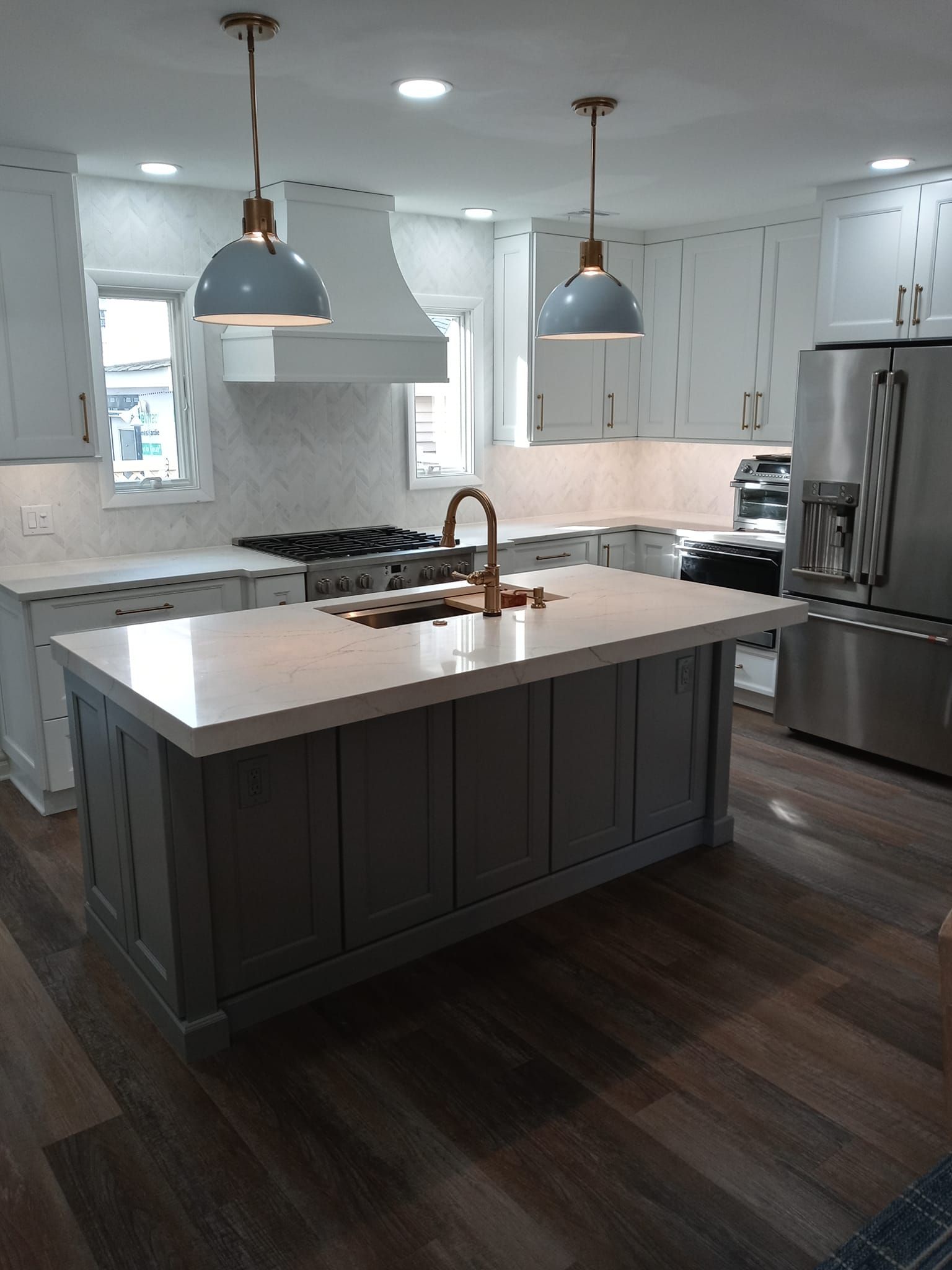 Modern kitchen with gray island, white cabinets, stainless steel appliances, and pendant lights.