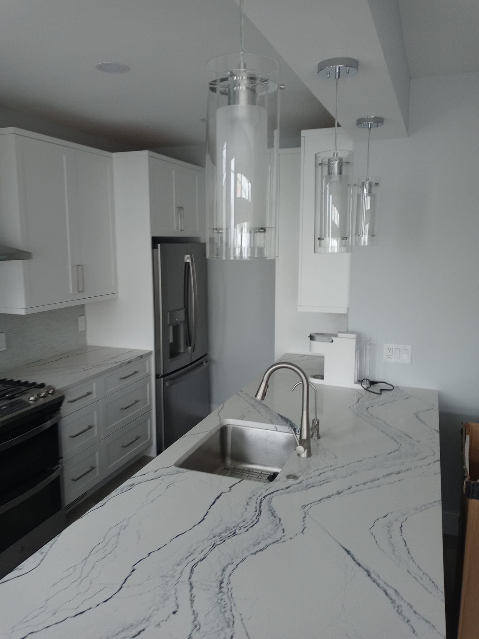 Modern kitchen with white cabinets, stainless steel appliances, and a marble countertop island with pendant lights overhead.