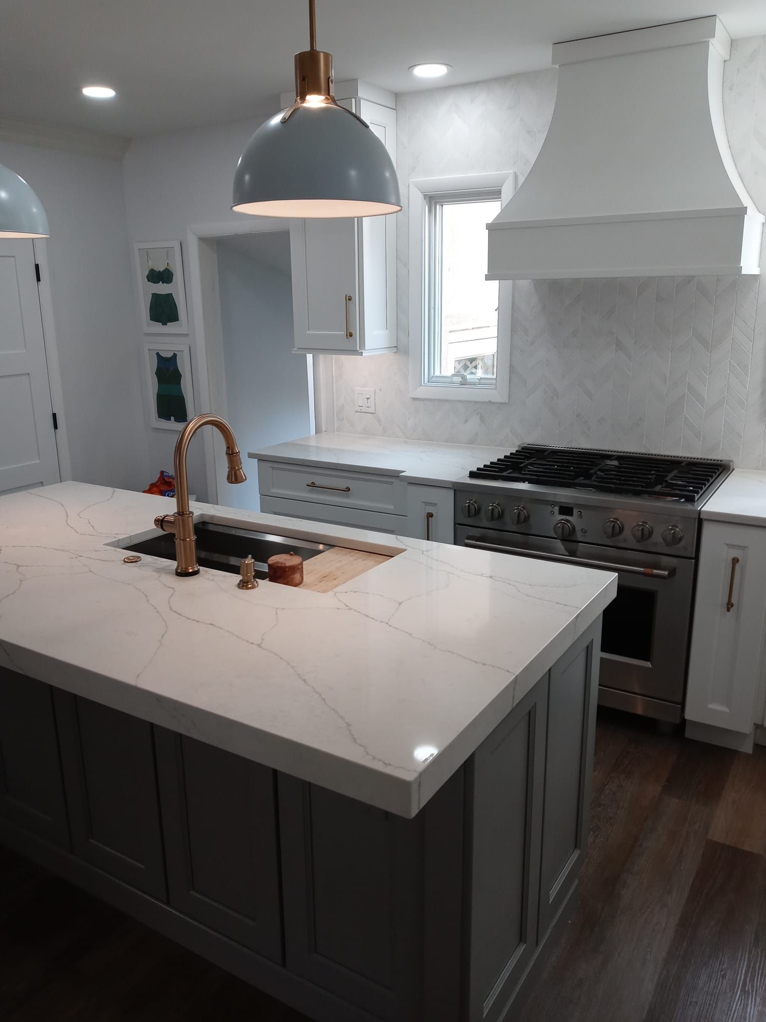 Kitchen with gray island, white countertops, stove, range hood, and blue pendant lights.