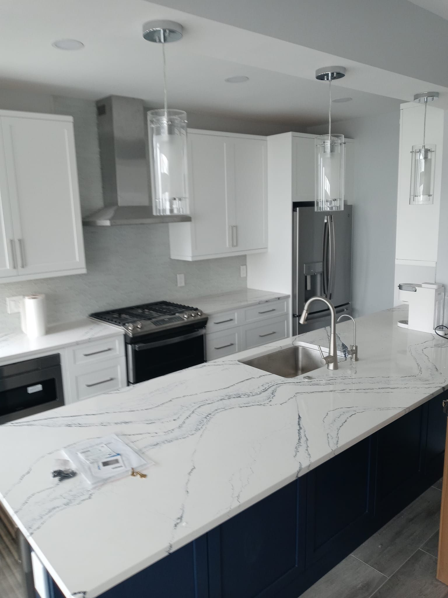 Modern kitchen with white cabinets, dark blue island, stainless steel appliances, and pendant lights.