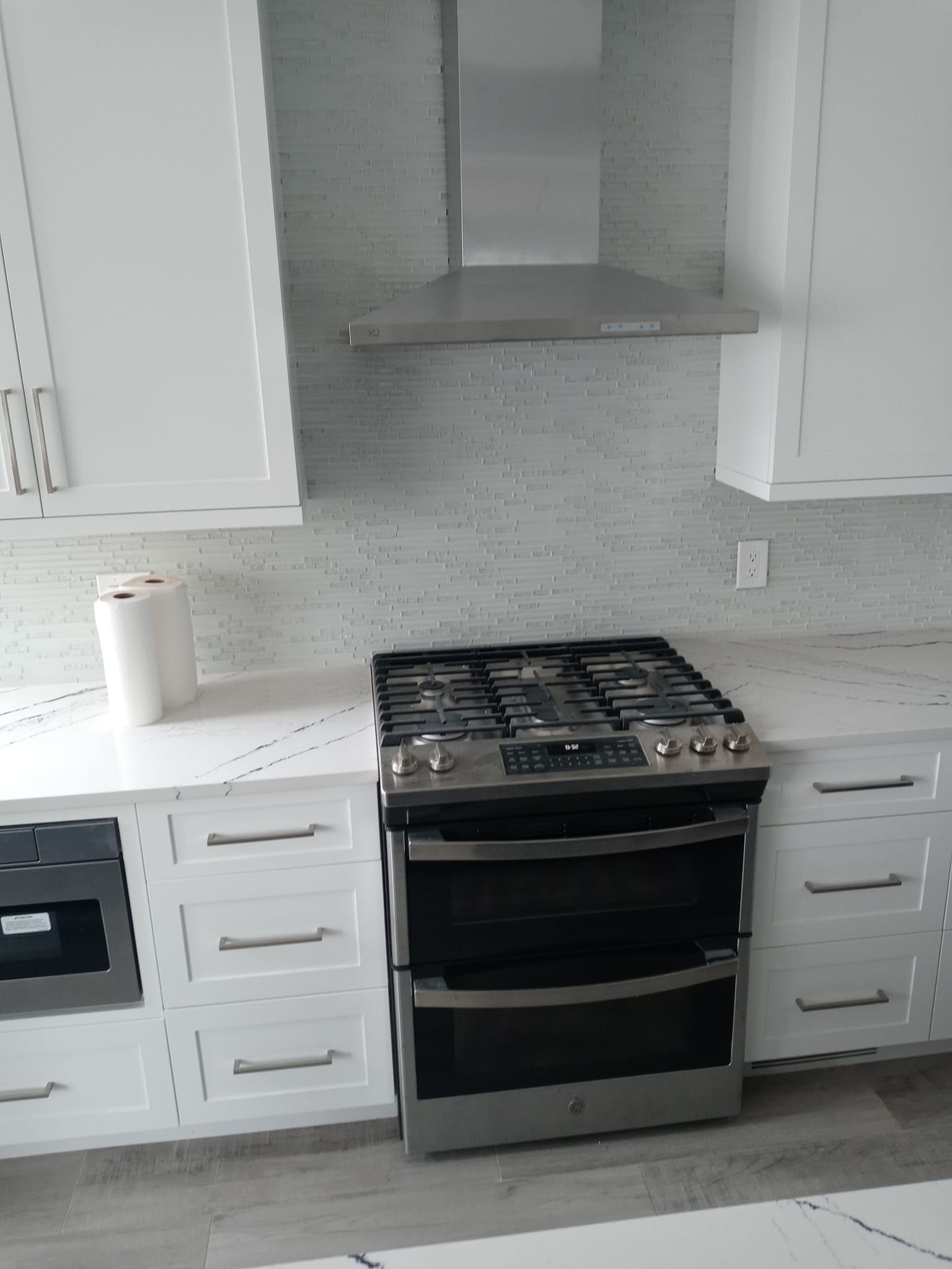 Kitchen with white cabinets, stainless steel range and hood, and light-colored backsplash.