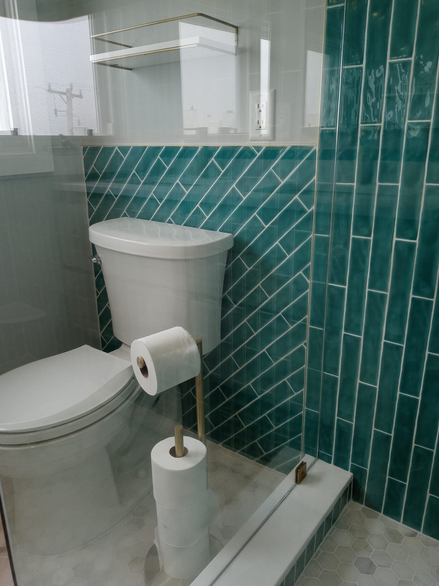 Bathroom with a white toilet, teal tiled walls, and gold toilet paper holder.