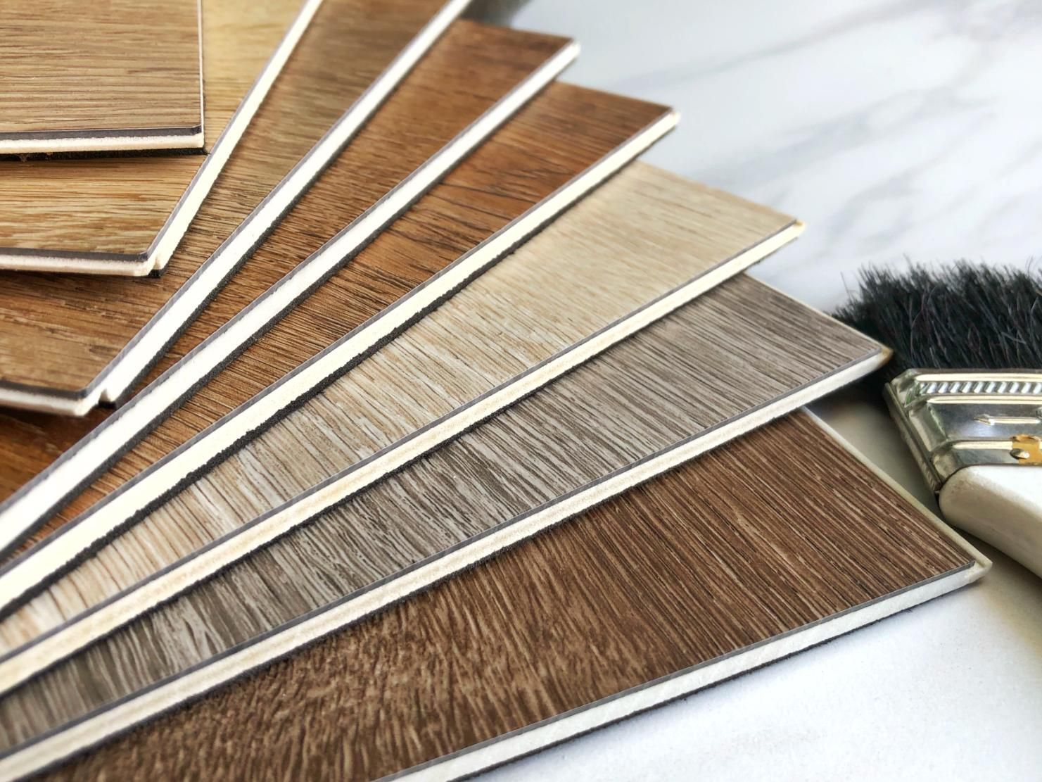 Wooden flooring samples in various shades, fanned out, beside a paintbrush.