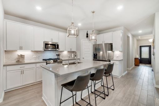 Modern white kitchen with island and three bar stools, stainless steel appliances, and wood floor.