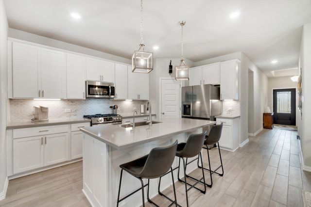 Modern white kitchen with island and three bar stools, stainless steel appliances, and wood floor.