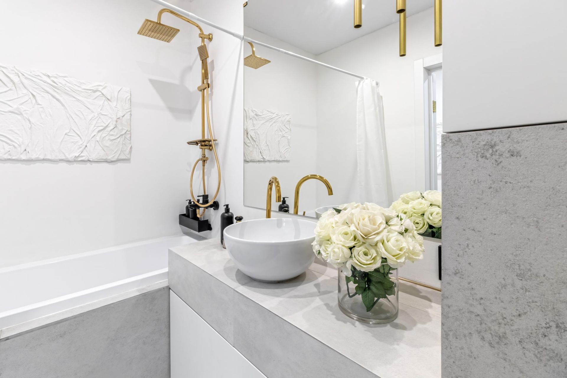 Modern bathroom with gold fixtures, white sink, and flowers.