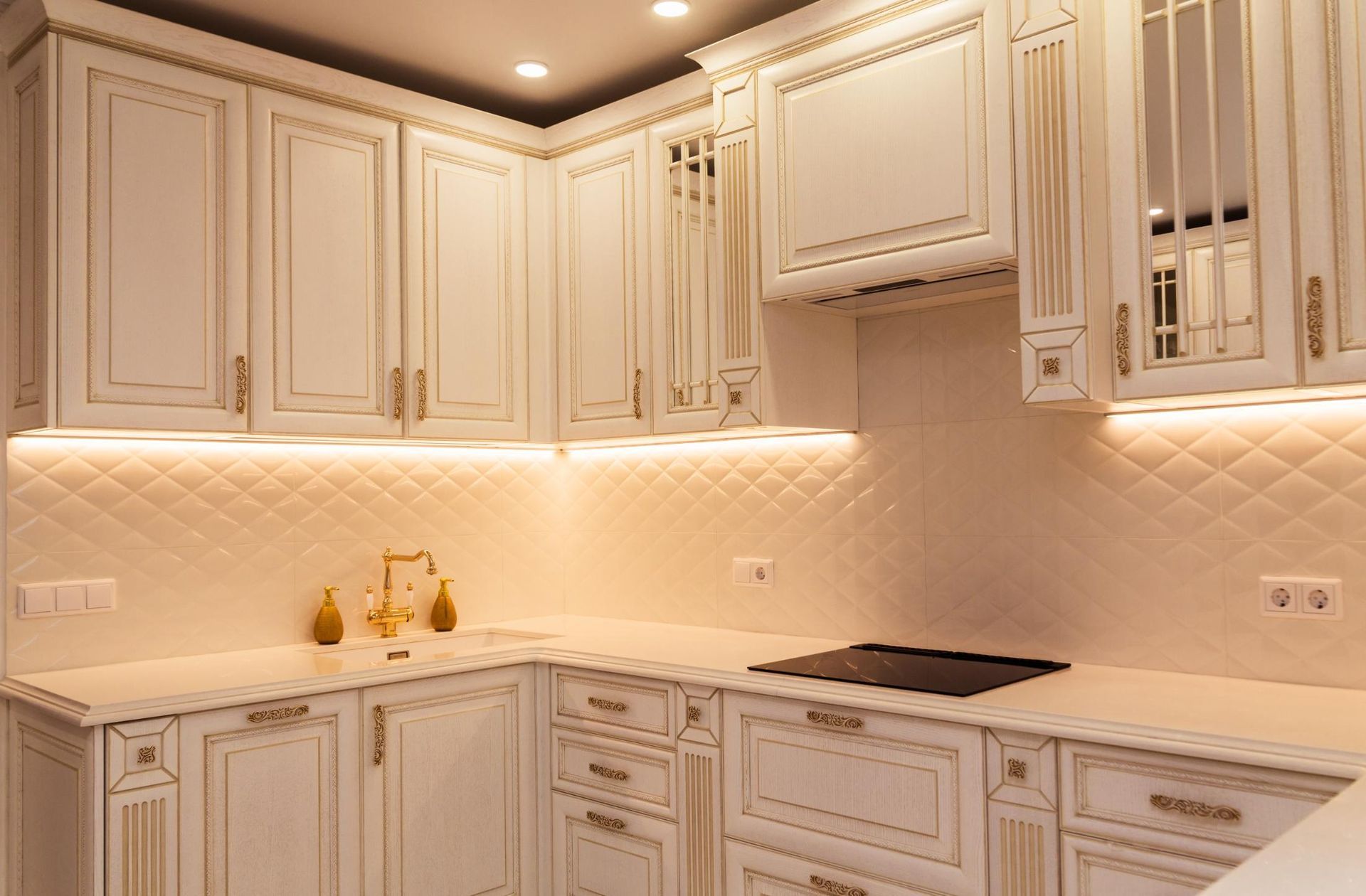 White kitchen with ornate cabinetry, gold accents, and under-cabinet lighting.
