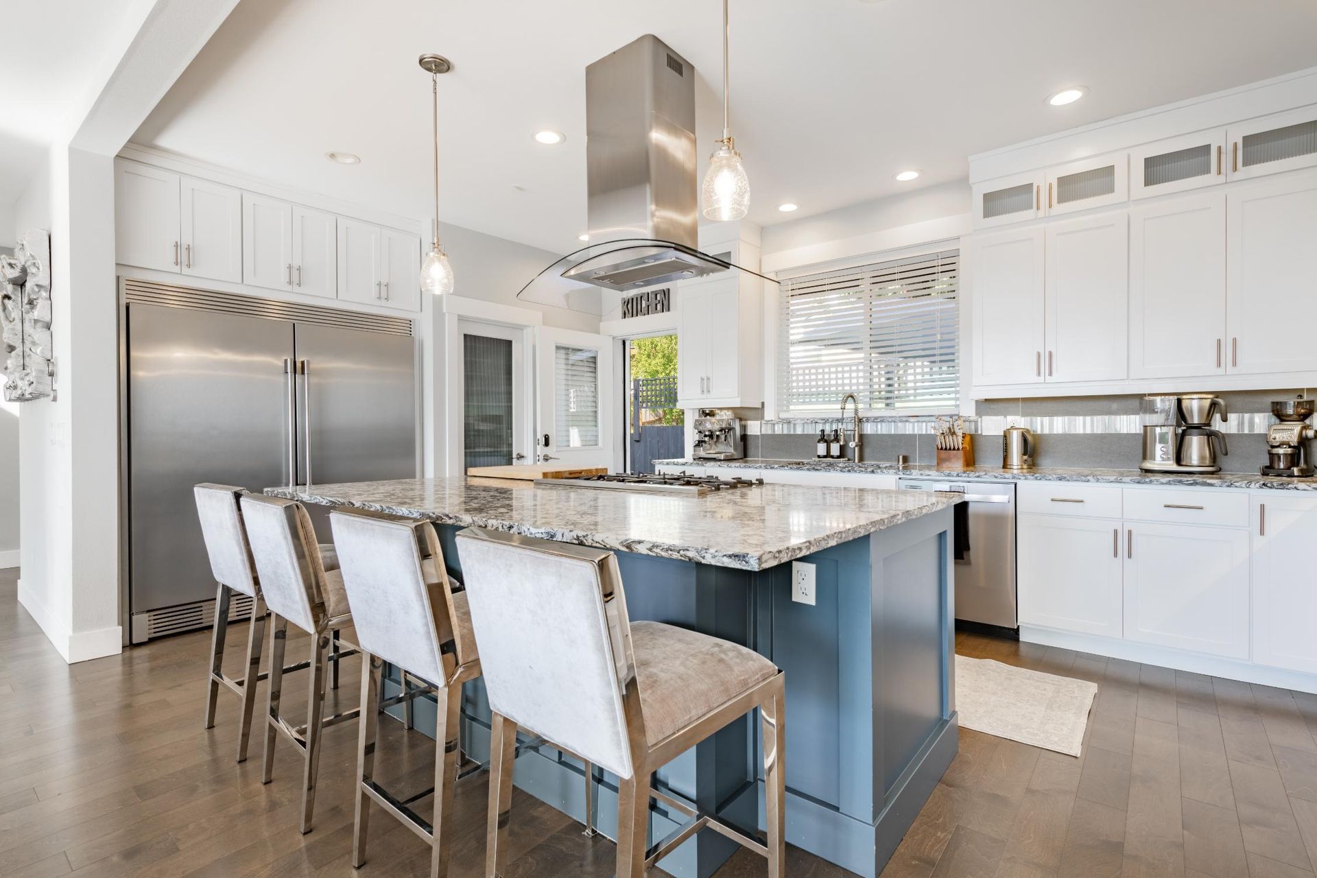 Spacious kitchen with blue island, stainless steel appliances, white cabinets, and bar stools.
