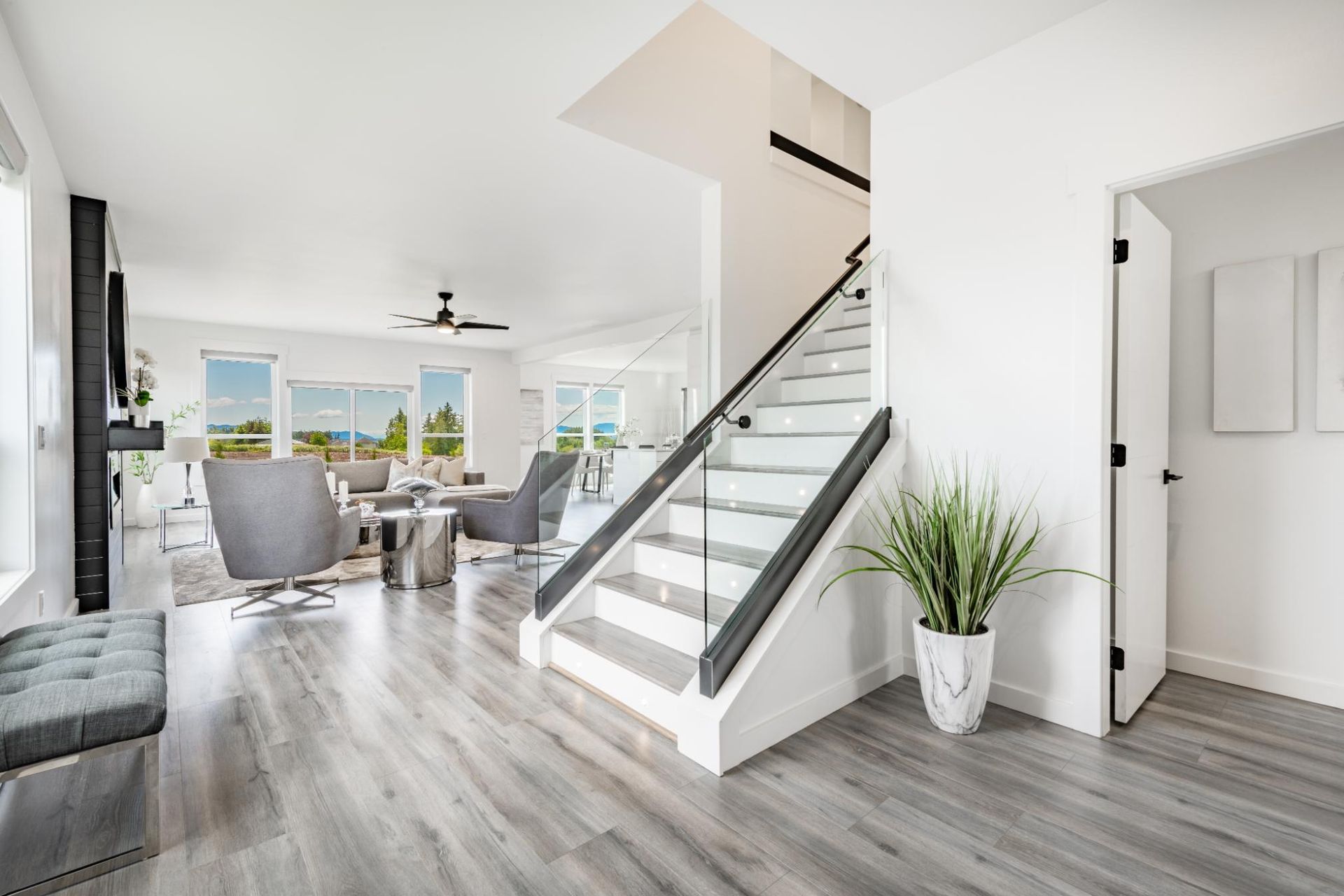 Spacious, bright interior with stairs, gray flooring, and a view of a living area with furniture and windows.