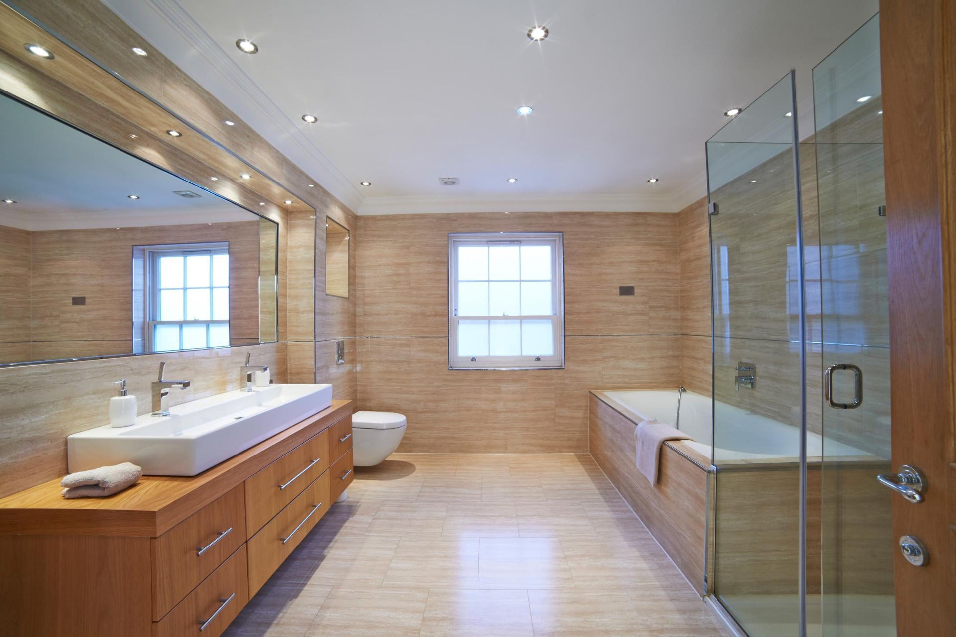 Spacious modern bathroom with wood vanity, large mirror, glass shower, and tub.