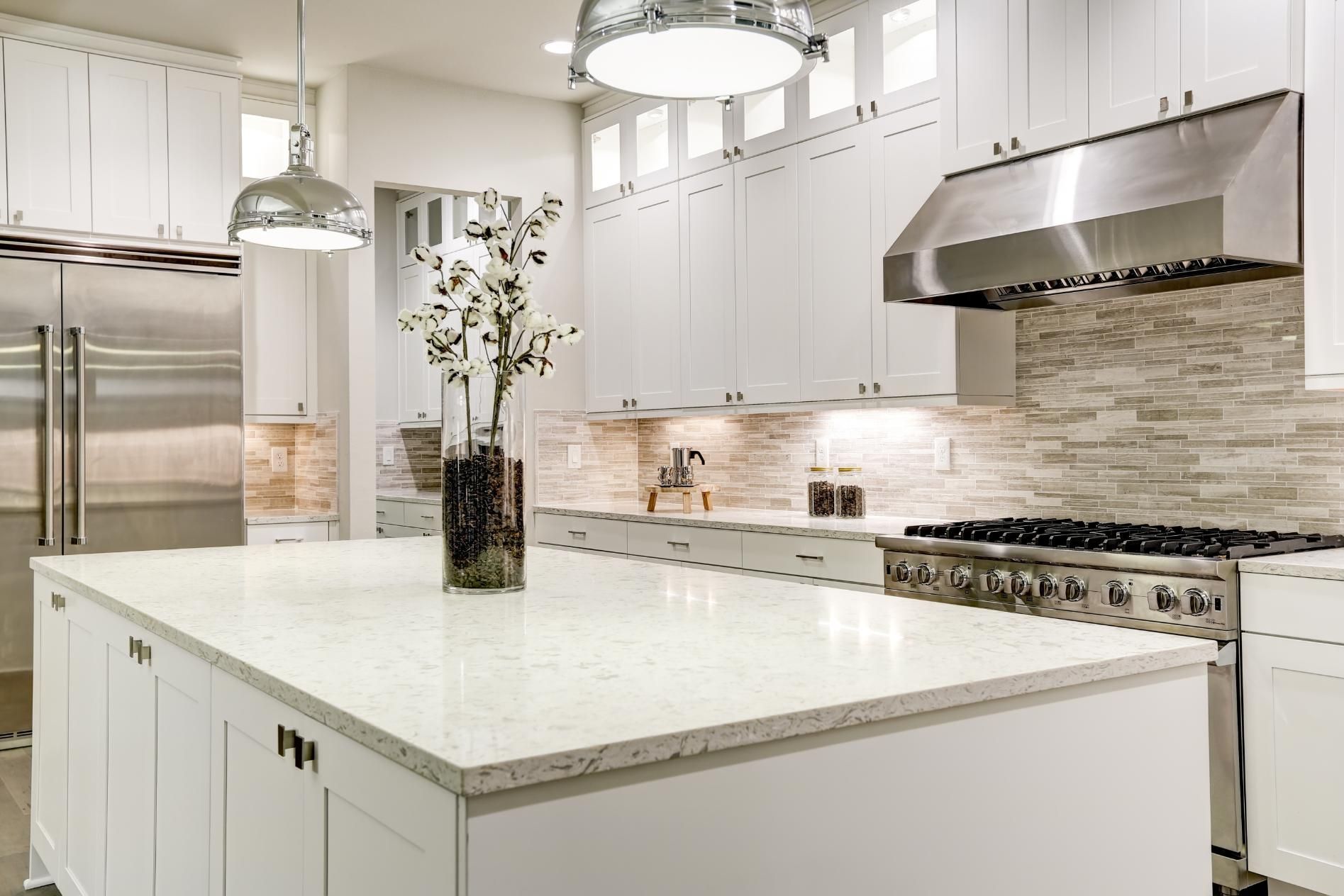 White kitchen with island, stainless steel appliances, and decorative flowers.