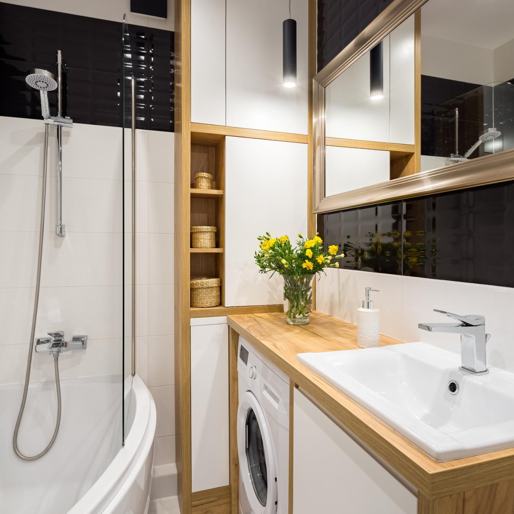 Bathroom with white and black tile, wooden accents, including a countertop, cabinets, and a built-in washing machine.