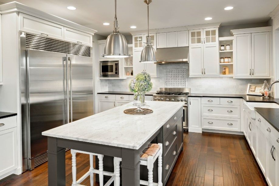Spacious white kitchen with dark gray island and stainless steel appliances.