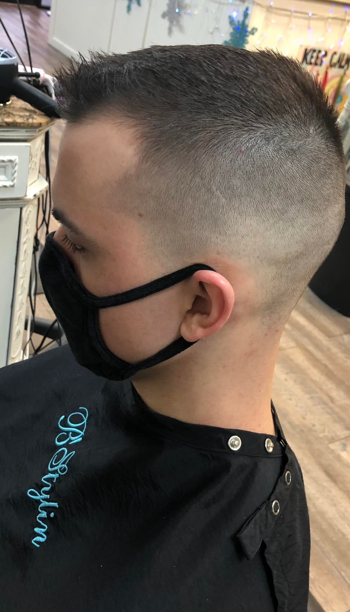 A man wearing a mask is getting his hair cut at a barber shop.